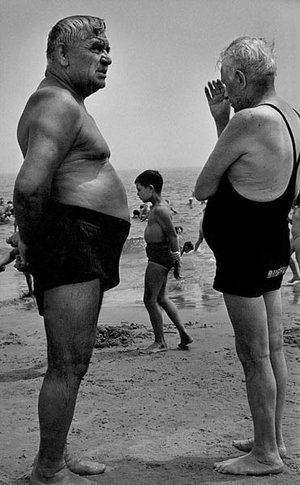 Two men stand on the beach talking while a boy walks by making a similar gesture, Coney Island, New York, 1950, Courtesy Galerie Thierry Bigaignon.